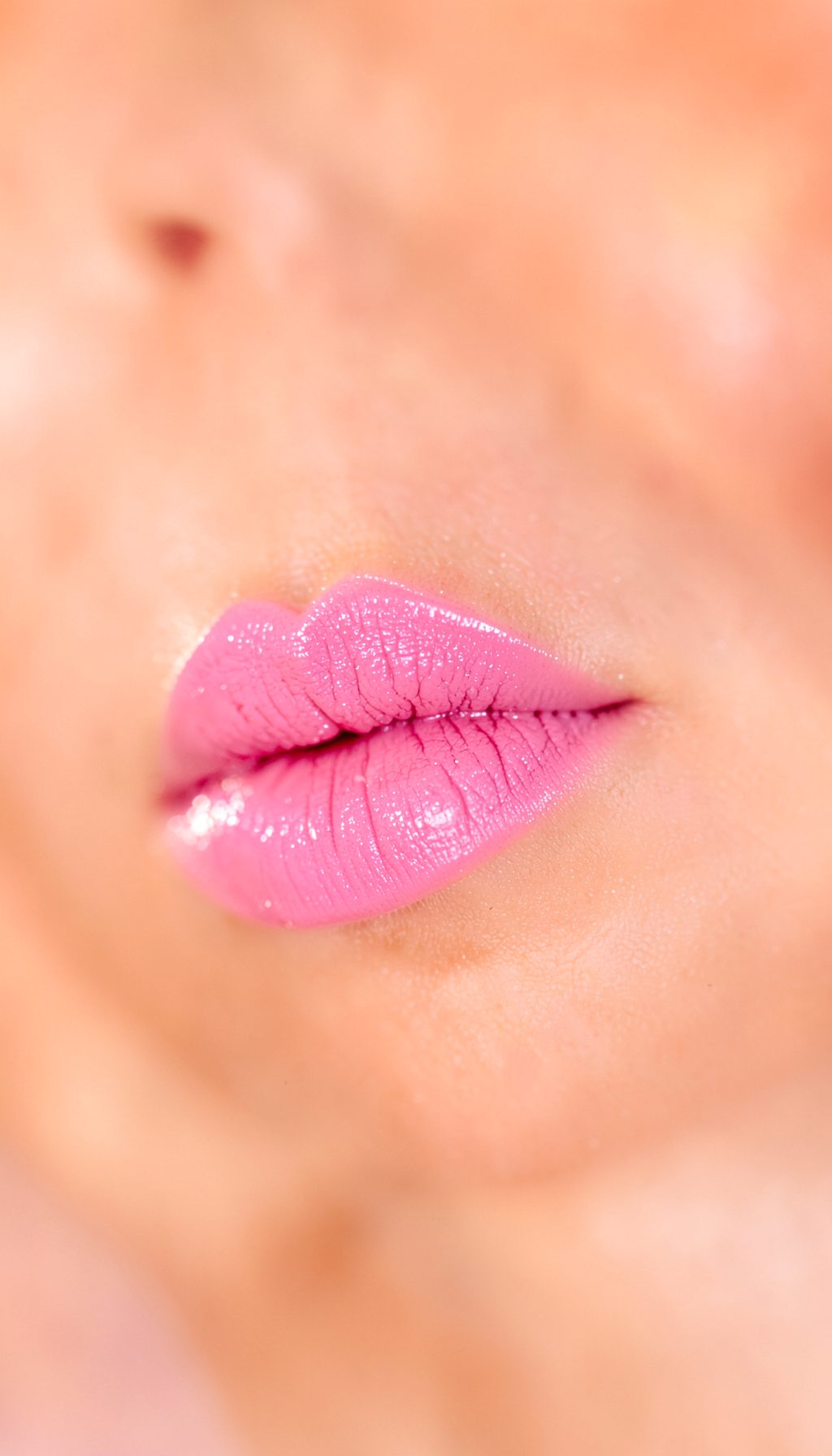 Batom rosa vibrante sobre fundo desfocado em tons quentes de pêssego e blush, clima editorial de beleza